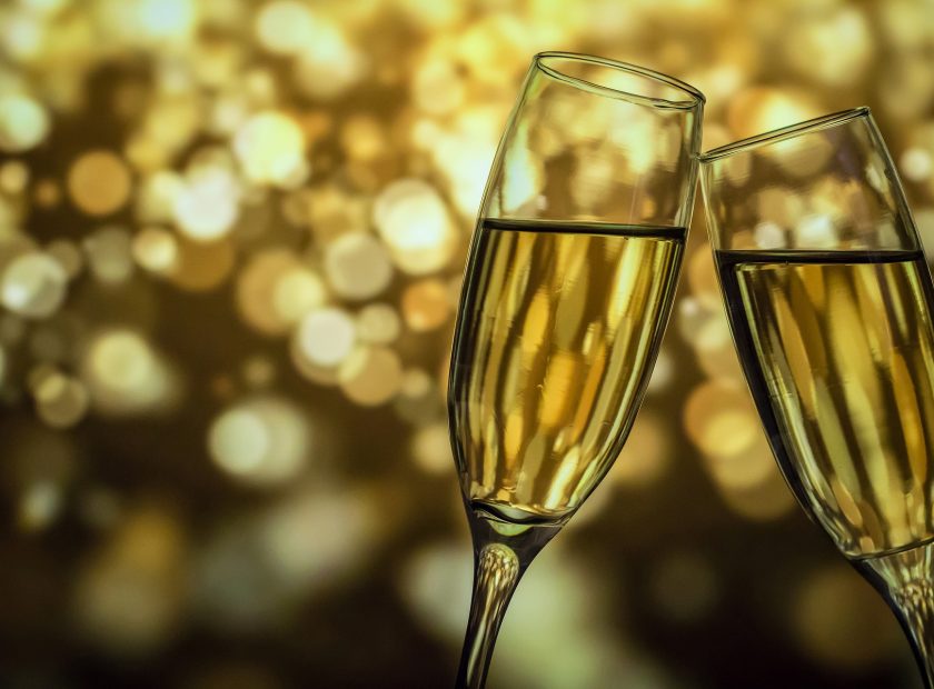 Two champagne flutes, touching at the top, with a sparkling light background