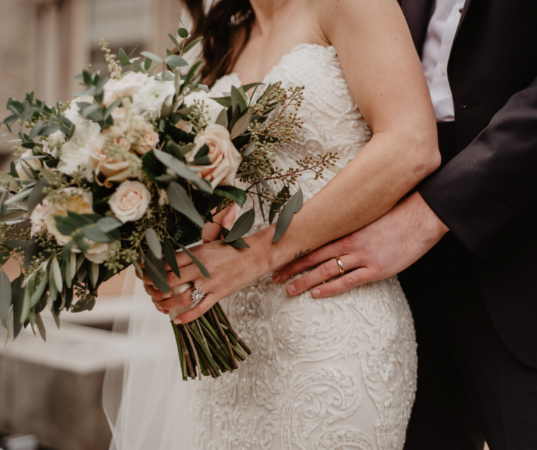 Close up of wedding couple, groom behind bride with his hand on her hip, and the bride holding a bouquet